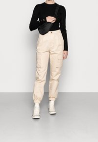 Pantalones cargo beige con puños elásticos, dos bolsillos laterales y un top negro de manga larga acanalado. Combinado con zapatillas blancas de caña alta.