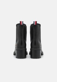 Botas de cuero negras hasta el tobillo con un tacón cuadrado alto, que presentan rayas de acento en rojo, blanco y azul en la lengüeta y una suela texturizada.