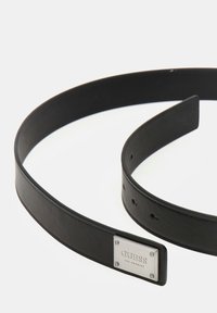 Juodas odinis diržas su lygia tekstūra, turintis sidabrinę stačiakampę sagtį, įspaustą užrašu "GUESS LOS ANGELES." Kelios skylės dydžiui reguliuoti.