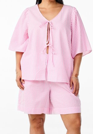 Vrouw draagt een los vallende top met verticale roze-witte strepen, striksluitingen en bijpassende knielange short.