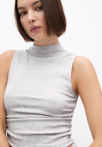 Graues ärmelloses Rollkragenoberteil aus weichem Stoff, taillierter Schnitt mit gerafften Seiten, glatte Textur, minimalistischer Stil.