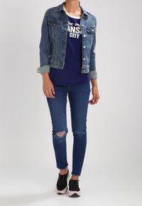 Jeansjacka i ljusblått, utrustad med bröstfickor. Marinblå t-shirt med djärv vit text. Mörkblå rivna skinny jeans. Svarta sneakers med rosa detaljer.