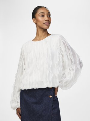 Weiße, strukturierte Bluse mit Rüschendetails, langen Puffärmeln und rundem Ausschnitt, kombiniert mit einem dunkelblauen Denimrock mit Knopfakzenten.