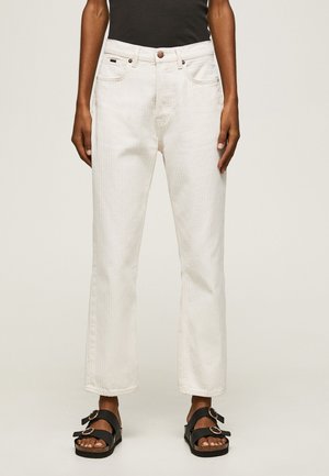 Osoba oblečená v vysokom páse, rovnom nohavicovom bielom džínse s jemnými vertikálnymi pruhmi, čiernom bezrukávovom topu a čiernych sandáloch s prackami.