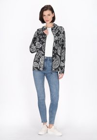 Jachetă neagră cu model paisley alb, cu închidere cu fermoar și glugă. Asortată cu blugi skinny albaștri și adidași albi. Textură de țesătură netedă.
