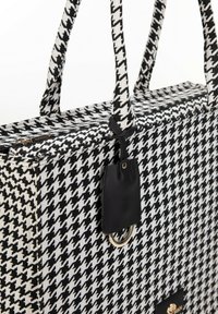Borsa tote con motivo a scacchi bianco e nero realizzata in tessuto testurizzato, dotata di due manici robusti, un accento in pelle nera e un logo dorato.