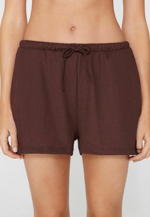 Shorts en tissu marron texturé avec ceinture élastique et lien à l'avant, portés par une personne debout avec les mains détendues le long du corps.