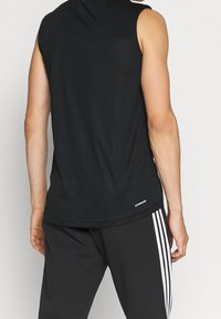 Débardeur noir à encolure arrondie en tissu doux et respirant. Présente un logo à l'ourlet, accompagné d'un pantalon noir avec des rayures blanches.