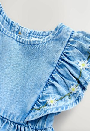 Világoskék árnyalatú farmerruházat fodros ujjakkal és hímzett fehér margarétákkal a nyakkivágás mentén. Kerek nyakkivágású és lágy tapintású anyagból készült.