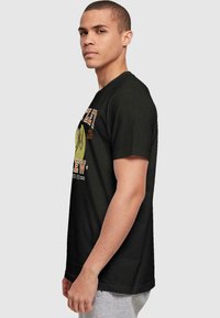 Black cotton t-shirt featuring graphic print with yellow and orange accents. Short sleeves and round neckline. Model shown in profile.