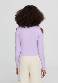 Top a maniche lunghe color lilla con spacchi sulle spalle, texture a coste, design corto e orlo delle maniche sfrangiato, indossato con pantaloni beige chiaro.