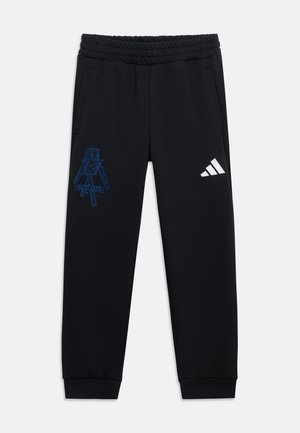 Pantalon de survêtement noir avec taille élastique, poignets côtelés, motif pixelisé de robot bleu sur la cuisse gauche et logo Adidas blanc sur la cuisse droite.