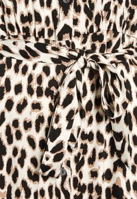 Leopardi-kuosiset kangas vaalealla taustalla, jossa on mustia ja ruskeita pilkkuja, kietoutuva vyötärö sidottavalla vyöllä sekä nappit yksityiskohtana.