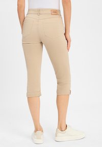 Beige cropped broeken met opgerolde manchetten en een verhoogd achterpand-label. Fijne, elastische stof; twee achterzakken zichtbaar.