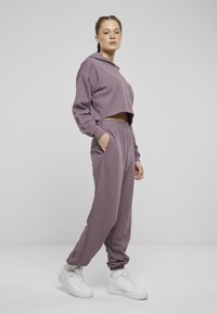 Felpa cortata viola e pantaloni della tuta abbinati realizzati in morbido tessuto. Design con cappuccio, cintura elastica e polsini affusolati. Sneakers bianche.