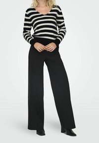 Pull à rayures noires et blanches avec un col en V, en matière douce et texturée, assorti à un pantalon noir taille haute à jambes larges et des talons noirs.