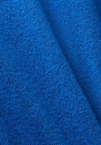 Gros plan sur un tissu bleu doux et texturé avec un pli diagonal révélant son motif tricoté et sa surface moelleuse.