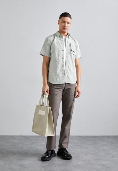Lysegrøn kortærmet skjorte med brystlomme, beige cargo-bukser og en struktureret beige tote taske. Sorte snørebåndssko. Minimalistisk design.