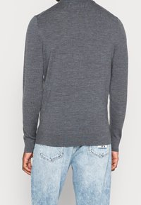 Pull gris à manches longues avec texture côtelée, silhouette ajustée et ourlet arrondi, porté avec un jean bleu clair légèrement délavé.