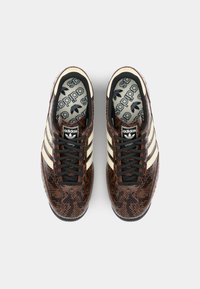 Sneaker Adidas con stampa pitonata marrone, strisce crema, lacci neri e soletta con marchio; forma compatta con finitura testurizzata.