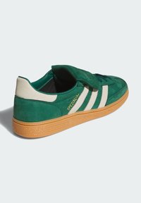 Green suede Adidas sneaker with white stripes, beige heel tab, gum sole, and gold "Spezial" logo on side, viewed from back side.
