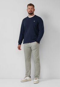 Sweatshirt bleu marine à col rond avec des accents de col blanc, associé à un pantalon vert clair et des baskets blanches. Design simple et coupe décontractée.