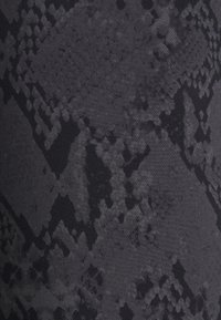 Černá textura látky má jemný geometrický vzor připomínající šupiny, s různými odstíny černé, které vytvářejí hloubku a kontrast.