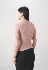 Rosa, strukturierte Langarmbluse mit taillierter Silhouette und Rundhalsausschnitt, kombiniert mit einem schwarzen Rock. Minimalistisches Design, keine sichtbaren Beschläge.
