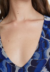 Tissu bleu à motifs avec un design en V, présentant des formes abstraites dans différentes nuances de bleu et de noir, mettant en avant la texture et le détail.