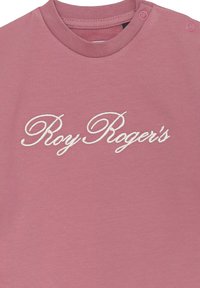 T-shirt in cotone rosa con collo a giro e il testo ricamato "Roy Roger's" in bianco sulla parte anteriore. Due bottoni a pressione sulla spalla.