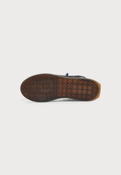 Semelle de chaussure avec une bande de roulement en caoutchouc texturé incluant des motifs circulaires et rectangulaires pour l'adhérence, affichée sur un fond clair uni.
