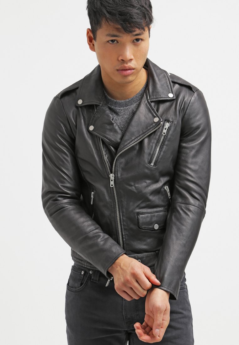 Zwarte leren motorjack met zilveren hardware, asymmetrische rits en twee voorkruiden. Dragen over een grijs shirt, nauwsluitend.
