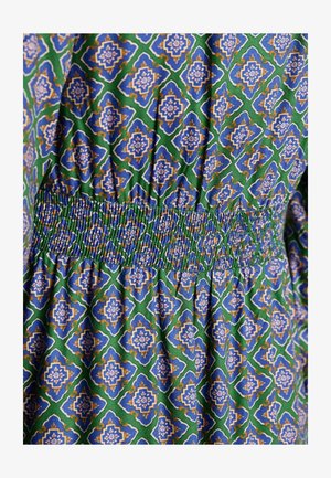 Kuvioitu puuvillakangas, jossa on vihreä tausta ja sinisiä, valkoisia sekä kultaisia geometrisia kuvioita. Rypytetty smokkivyötärö lisää tekstuuria.