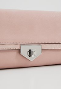 Měkká růžová kožená kabelka s texturovaným pásem a stříbrným geometrickým zámkem uprostřed přední strany.