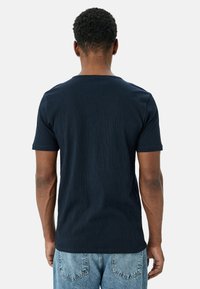 Marineblå t-shirt med kortærmer, med et struktureret mønster, rund hals og en let tapered pasform, parret med lysevaskejeans.