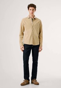 Beež pika varrukaga särk ees taskuga, kombineeritud tumeliste siniste teksade ja pruunide kingadega, millel on nööbitav disain ja krae.