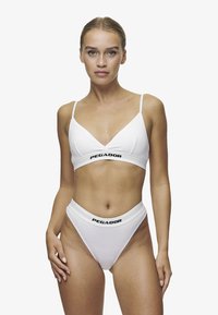 Bralette blanche et culottes taille haute avec une bande logo noire "PEGADOR". Tissu doux et lisse avec un design minimaliste et des formes triangulaires.