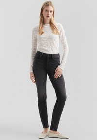 Witte lange mouwen kanttop gecombineerd met hoog-was zwarte skinny jeans. Schoeisel bestaat uit lichtgekleurde ballerina's met studs.