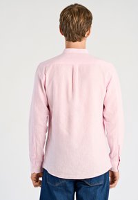 Roze shirt met lange mouwen en een button-downkraag, textuurrijk stof, enkele plooien aan de achterkant en manchetten met twee knopen, gedragen met een blauwe spijkerbroek.