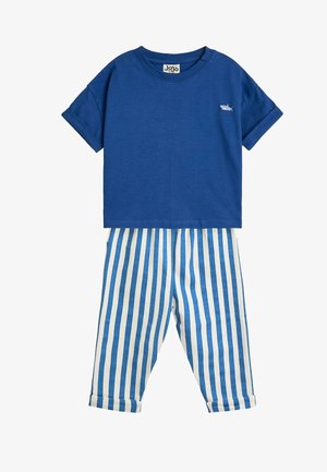 Kort blå t-shirt med lille hajbroderi kombineret med hvide og blå bukser med vertikale striber og foldede manchetter.