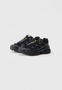 Sapatos de trail running pretos com um upper texturizado, atacadores em contraste e uma sola robusta para tração. Apresentam um design flexível e amortecimento.