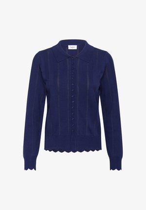 Tumedat sinise värvi kudumiga kardigan, millel on laineline ääreosa, krae ja nööpidega esikülg. Omab vertikaalseid triibudetaile ning pikki varrukasid, et tagada sobiv välimus.