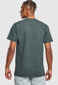 Mørkegrøn bomulds T-shirt med korte ærmer, rund hals og en glat tekstur. Har en ensfarvet ryg uden grafik eller detaljer.