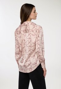 Blusa a maniche lunghe di un rosa chiaro, con un motivo a fiocco di un rosso intenso. Texture liscia con orlo arrotondato e dettagli sulla yolk posteriore.