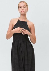 Black halter dress with smocked bodice and flowing skirt. Made of lightweight fabric with a textured check pattern. Minimalist design.