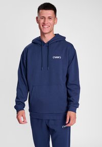 Mörkblå hoodie i mjukt material, med en framficka, dragsko på huvan och en liten logotyp på bröstet. Nederkantens mudd är ribbad.