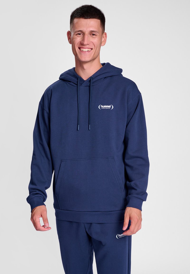 Mörkblå hoodie i mjukt material, med en framficka, dragsko på huvan och en liten logotyp på bröstet. Nederkantens mudd är ribbad.