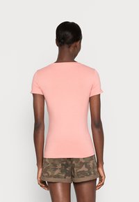 T-shirt aderente a maniche corte in cotone rosa chiaro con scollo rotondo. Abbinato a pantaloni corti con motivo camouflage.