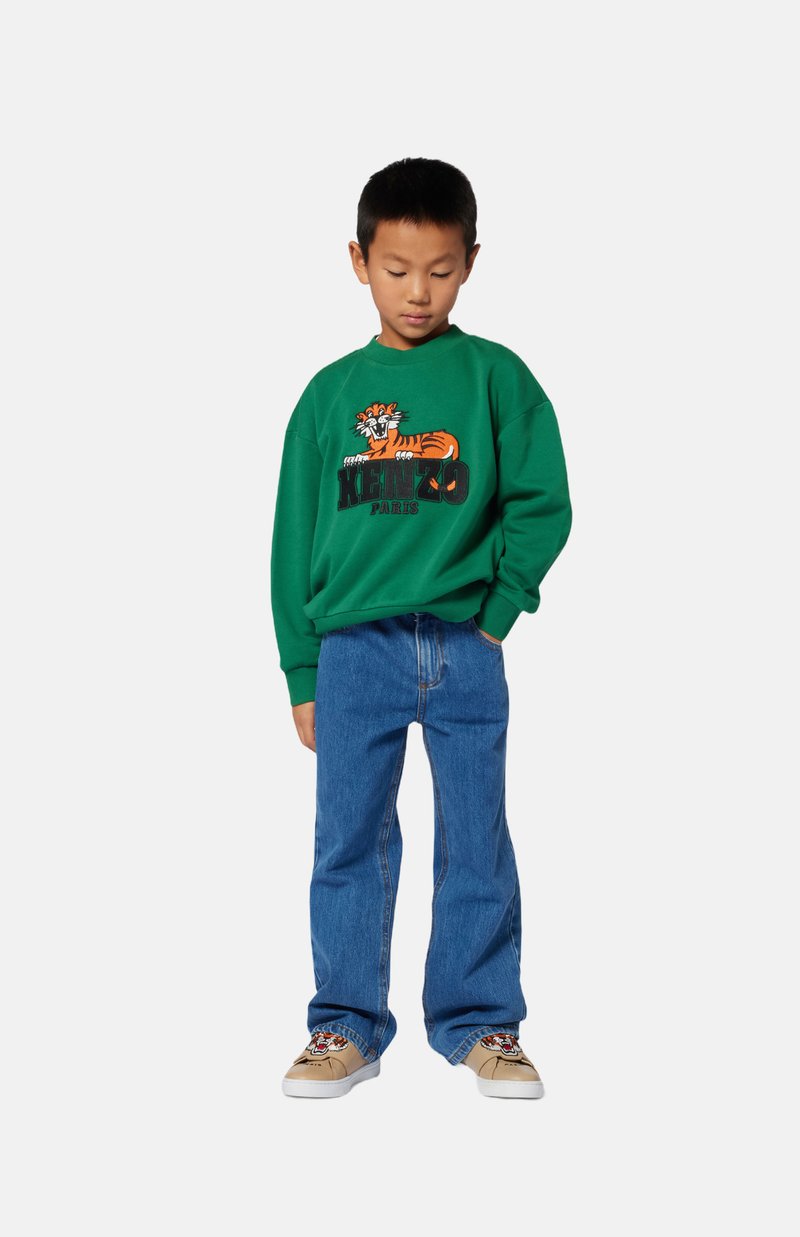 Sweatshirt vert avec un graphisme de tigre et le texte « KENZO PARIS », associé à un jean bleu et des baskets beiges avec un design de tigre.