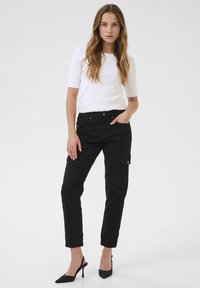 Pantalons cargo noirs avec poches latérales, jambes fuselées et ourlets aux chevilles, assortis d'un haut blanc à manches courtes et de chaussures à talons noires.